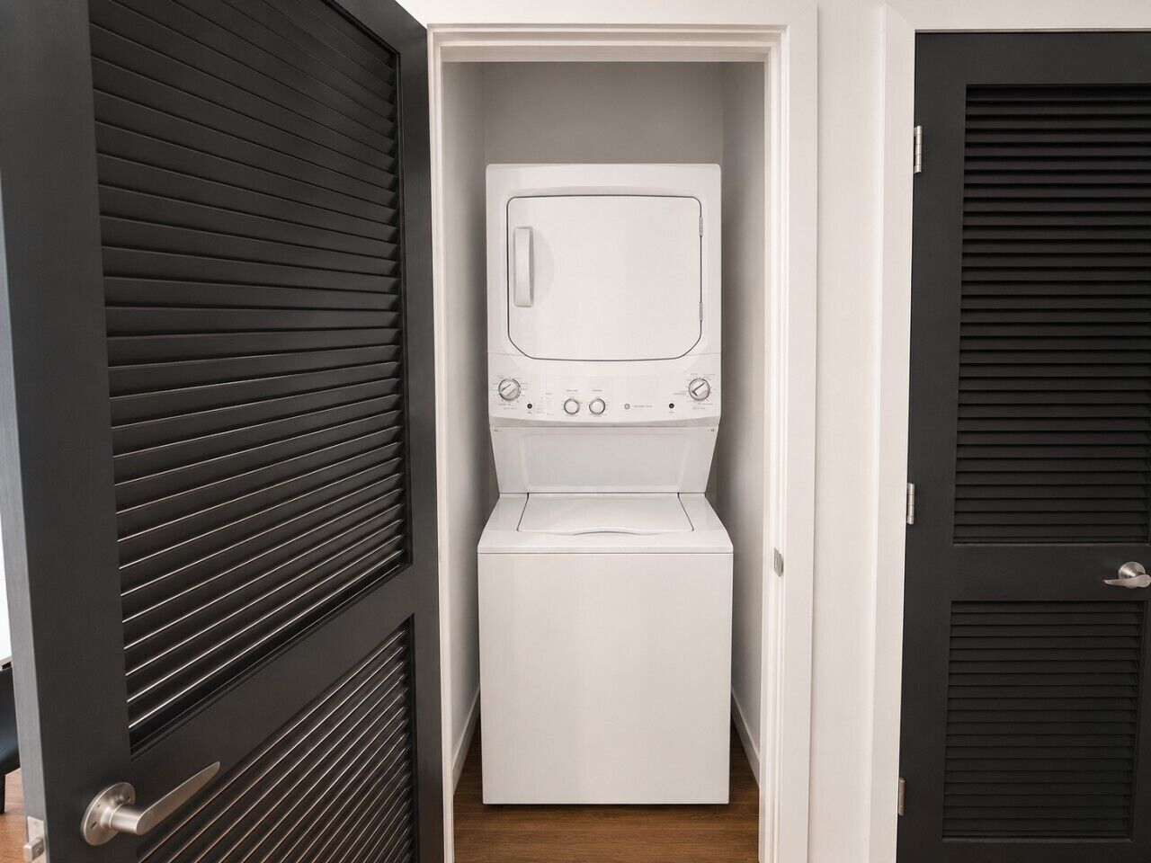 A compact laundry room with a washing machine and dryer, enclosed by a door with horizontal slats.