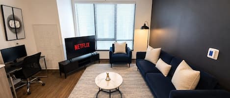 A modern living room with a dark blue sofa, a coffee table, a TV, and a ceiling fan.