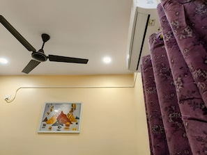 Un ventilador de sostre, un aparell d'aire condicionat, una cortina amb motius florals i una obra d'art emmarcada a la paret.