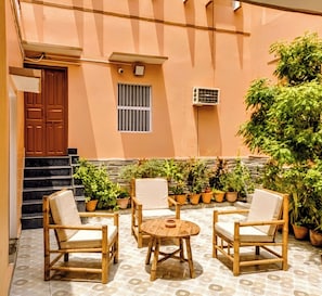 Un patio con mobiliario de madera, plantas en macetas y una escalera que lleva a la entrada.