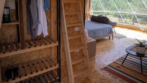 Une chambre avec un lit superposé, une échelle, une petite table et une vue sur l’extérieur grâce à une grande fenêtre.