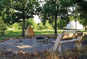 Un terrain de camping équipé d’un banc en bois, d’un foyer en pierre et d’une tente en forme de dôme.