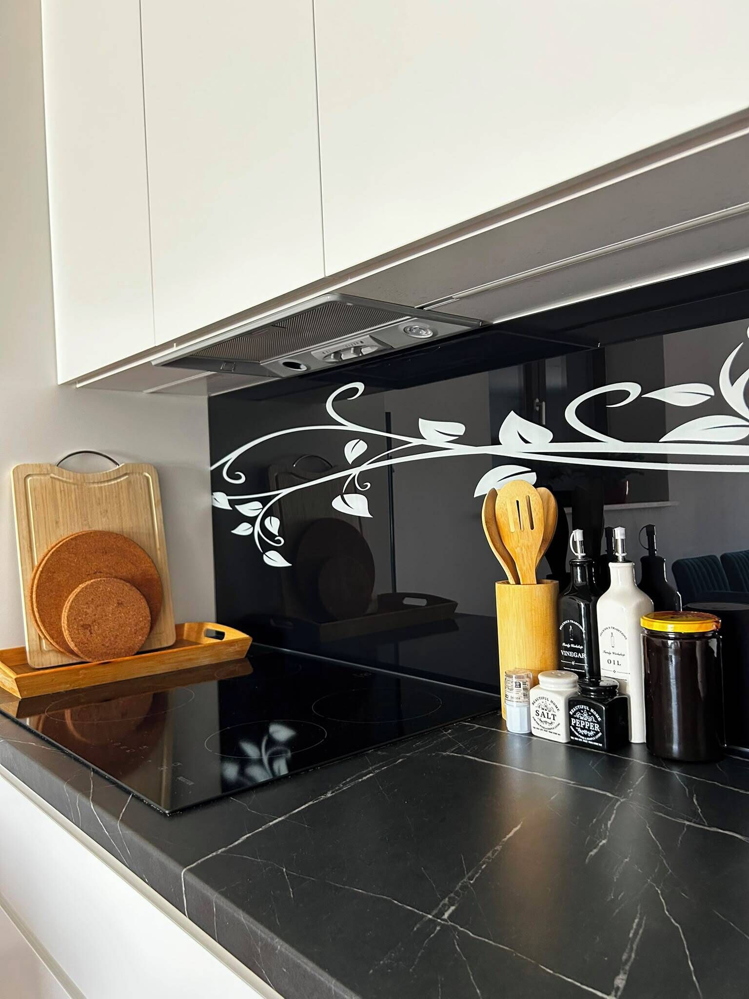 Cocina con encimera negra, tabla de cortar de madera y diversos utensilios y botellas.