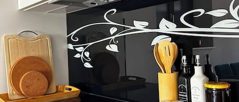 Cocina con encimera negra, tabla de cortar de madera y diversos utensilios y botellas.