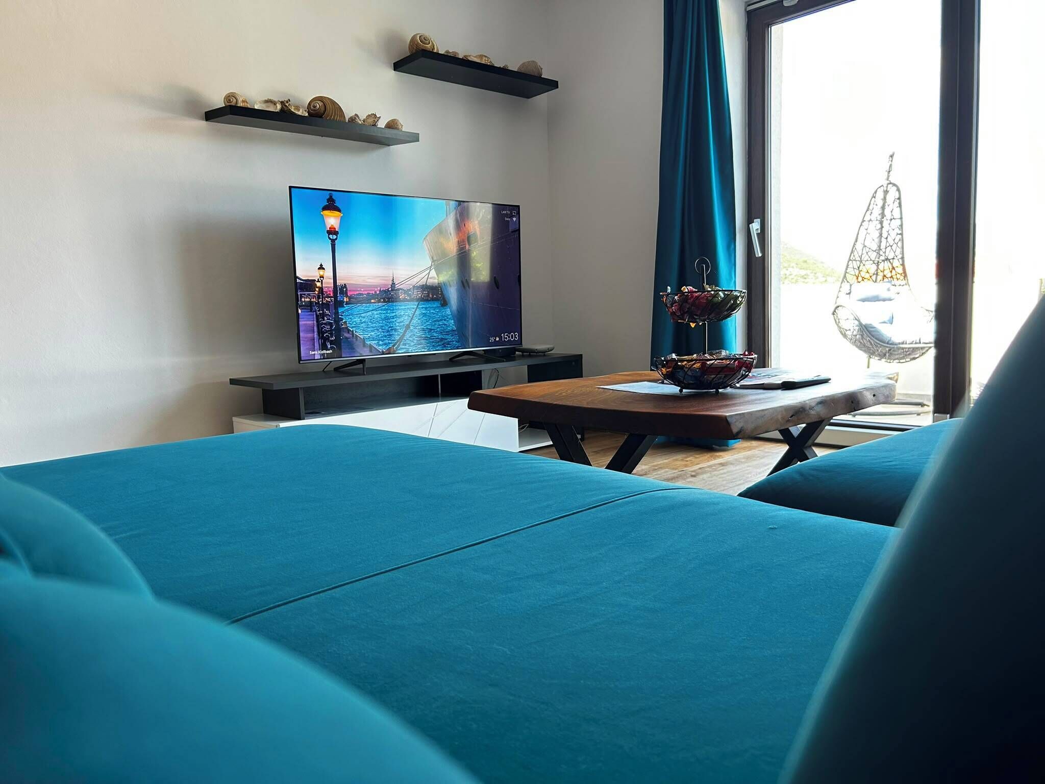 Een moderne woonkamer met een flatscreen televisie, smaragdgroene banken, een houten salontafel en decoratieve schelpen op planken.