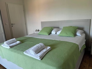 Een bed met een groen geweven sprei, twee witte handdoeken en twee groene kussens.