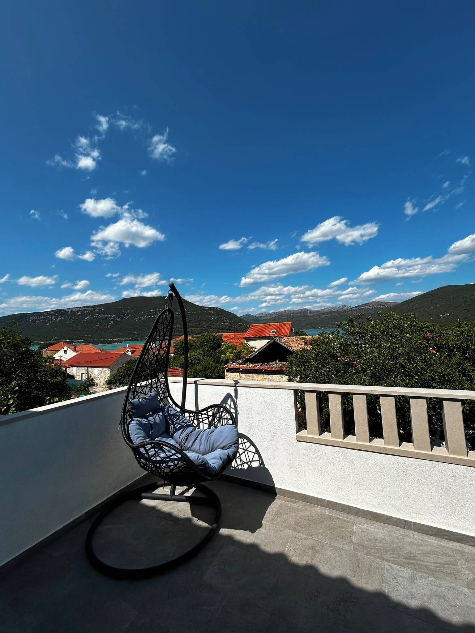 A balcony with a hanging chair, a view of a mountainous landscape, and a clear blue sky.