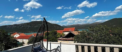 Ein Balkon mit einer Hängematte, Blick auf eine gebirgige Landschaft und einem strahlend blauen Himmel.