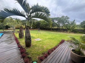 A backyard with a wooden deck, a lawn, and a variety of plants including palm trees. -  A  traditional, tropical Mauritian villa, 3-4 mins walk  to an amazing beach. (Balaclava)