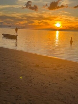 A beach scene with a boat and a person standing in the water during sunset. -  A  traditional, tropical Mauritian villa, 3-4 mins walk  to an amazing beach. (Balaclava)
