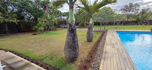 A backyard with a swimming pool, a wooden deck, and various tropical plants. -  A  traditional, tropical Mauritian villa, 3-4 mins walk  to an amazing beach. (Balaclava)