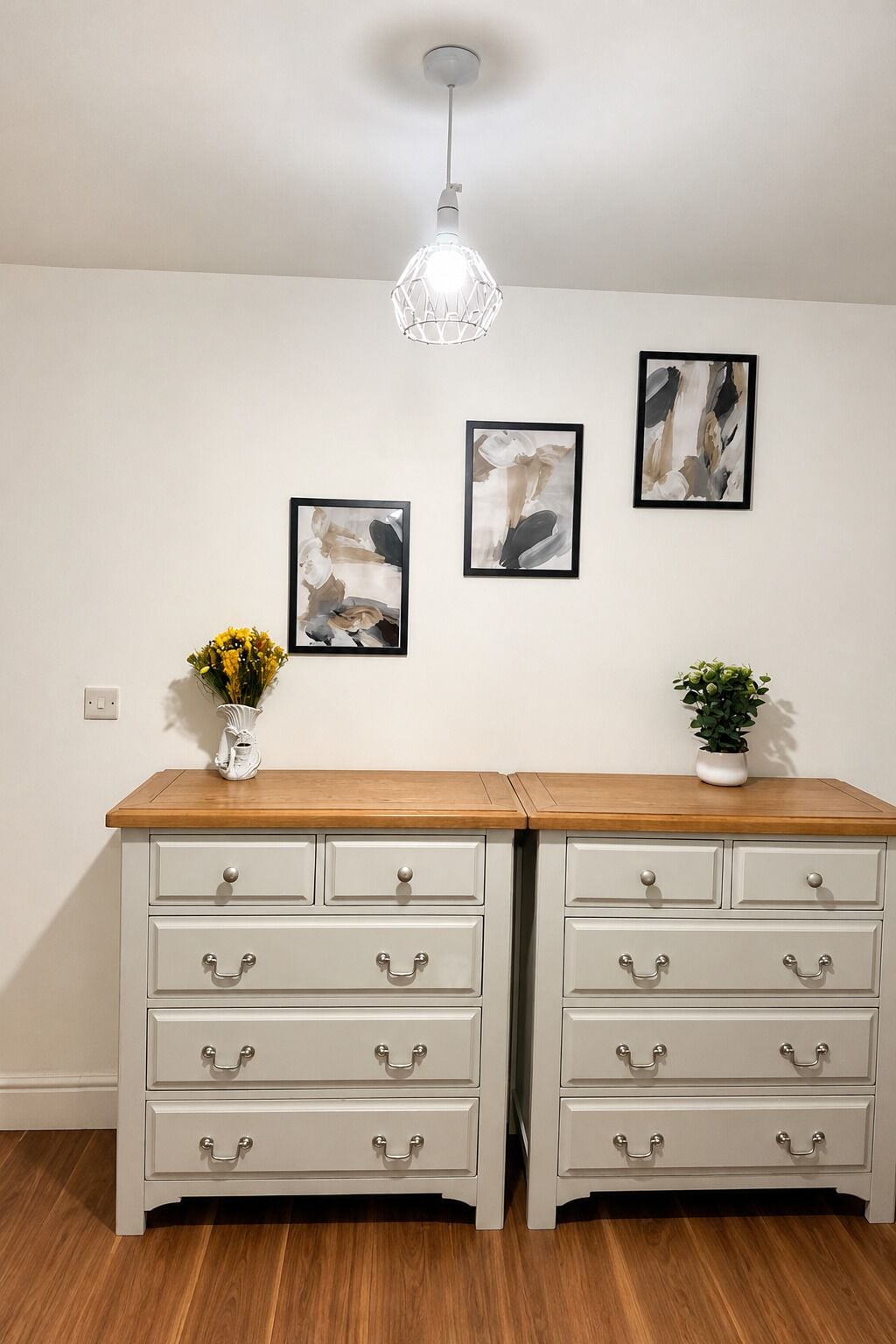 A room with a wooden dresser, two drawers, a vase with yellow flowers, and a potted plant.