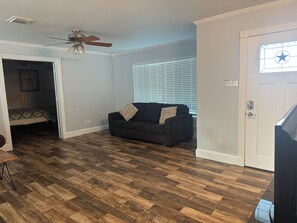 A living room with a dark-colored sofa, a ceiling fan, a wooden floor, and a door with a star-shaped window. - 3-bedroom 2-1/2 bath house in beautiful Galveston walk to the beach (Galveston)