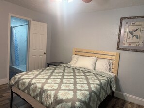 Ein Schlafzimmer mit einem Bett, einem Nachttisch, einer Tür und einem gerahmten Bild an der Wand.