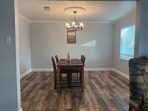 A dining area with a wooden table and chairs, a chandelier, and a window with blinds. - 3-bedroom 2-1/2 bath house in beautiful Galveston walk to the beach (Galveston)