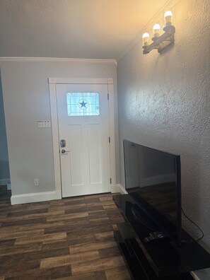 Ein Zimmer mit Holzdielenboden im Fischgrätmuster, einer weißen Tür mit sternförmigem Fenster und einem an der Wand befestigten Fernseher.