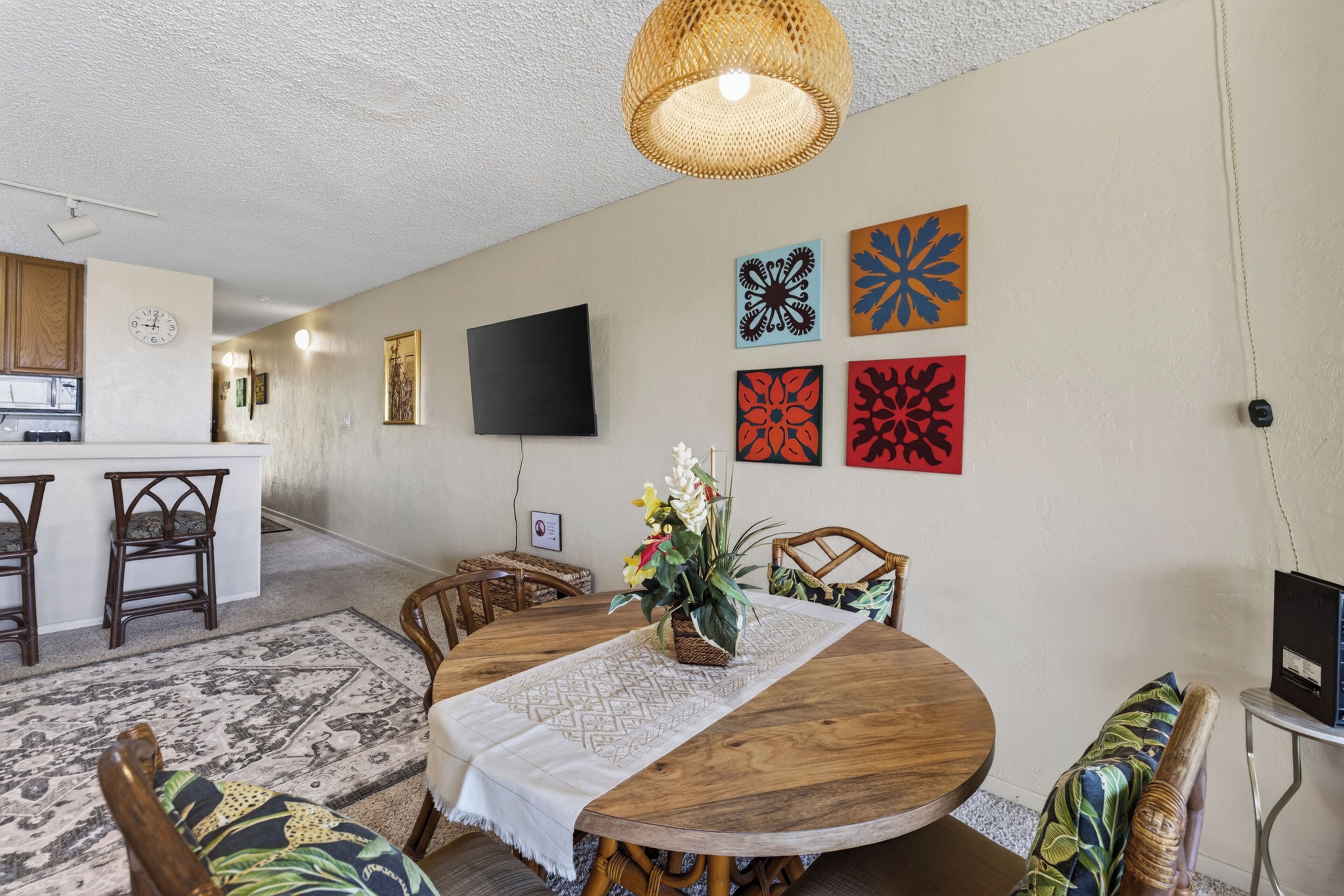 A dining area with a round wooden table, chairs, a woven light fixture, and wall art.