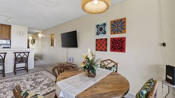 A dining area with a round wooden table, chairs, a woven light fixture, and wall art.