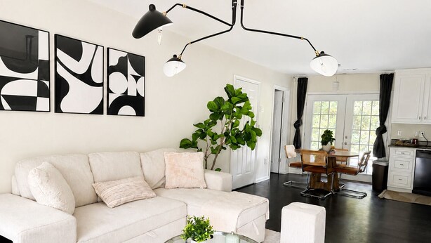 Een moderne woonkamer met een bank, een glazen salontafel en een eethoek met een tafel en stoelen.