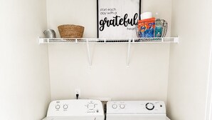 Een wasserette met twee witte voorladers, een plank boven met wasmiddelen, en een lijst met een inspirerende quote.