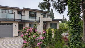 A modern two-story house with a stone facade, large windows, and a balcony. - Steps to Beach • 2BR White Rock Suite • Sleeps 4 (Surrey)