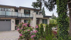 A modern two-story house with a stone facade, large windows, and a balcony. - Steps to Beach • 2BR White Rock Suite • Sleeps 4 (Surrey)