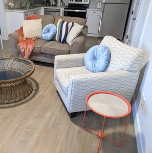 A living room with a sofa, a round wicker coffee table, and a red stool. - Steps to Beach • 2BR White Rock Suite • Sleeps 4 (Surrey)
