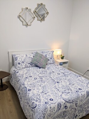 Un dormitorio con cama, mesita de noche, lámpara y dos espejos en la pared.