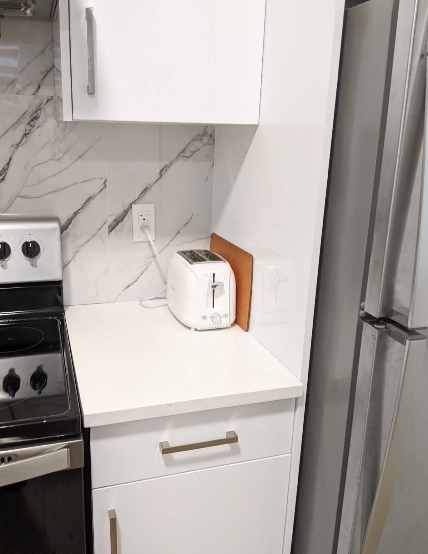 A kitchen with white cabinets, a toaster, a stove, and a refrigerator.