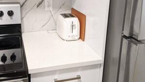 A kitchen with white cabinets, a toaster, a stove, and a refrigerator. - Steps to Beach • 2BR White Rock Suite • Sleeps 4 (Surrey)