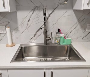 A stainless steel kitchen sink with a modern faucet, a paper towel holder, a soap dispenser, and a toothbrush holder. - Steps to Beach • 2BR White Rock Suite • Sleeps 4 (Surrey)