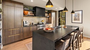 Une cuisine moderne avec des meubles de couleur bois foncé, un îlot central et des luminaires suspendus.