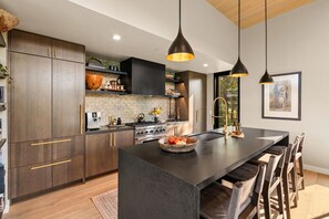 Une cuisine moderne avec des meubles de couleur bois foncé, un îlot central et des luminaires suspendus.
