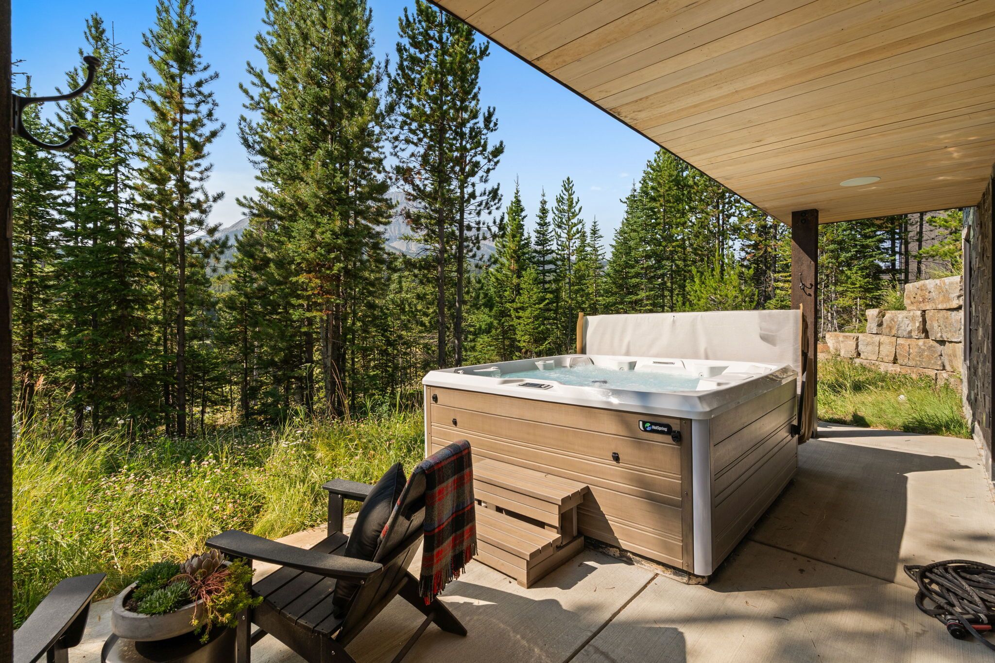 A hot tub with a wooden deck and a chair, surrounded by a forest.