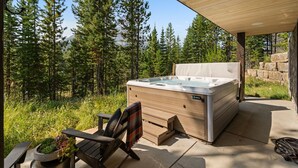 Un bain à remous avec une terrasse en bois et une chaise, le tout entouré d’une forêt.
