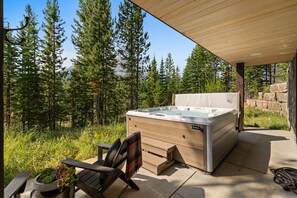 Un bain à remous avec une terrasse en bois et une chaise, le tout entouré d’une forêt.