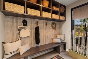 Une pièce avec un banc en bois, des étagères avec des paniers, un porte-manteau et une vue sur l’extérieur.