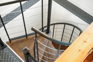 En spiralformet trappe med et trægelænder og metalspindsværk, der fører op til en etage med et fiskebensmønstret gulv.