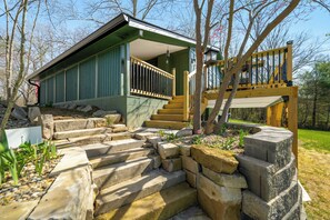 A two-story house with a green exterior, a wooden staircase leading to the upper level, and a small porch area. - Cozy 2-bedroom cottage in serene Brown County Indiana (Nashville)