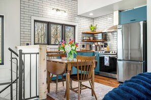 A modern kitchen with a dining area, featuring a stainless steel refrigerator, a built-in oven, and a wooden dining table with chairs. - Cozy 2-bedroom cottage in serene Brown County Indiana (Nashville)