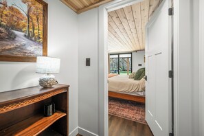A hallway leading to a bedroom with a bed, a nightstand, a lamp, and a painting on the wall. - Cozy 2-bedroom cottage in serene Brown County Indiana (Nashville)