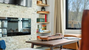Ein modernes Wohnzimmer mit Kamin, Bücherregalen und Blick auf Bäume durch das Fenster.