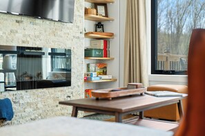 Ein modernes Wohnzimmer mit Kamin, Bücherregalen und Blick auf Bäume durch das Fenster.
