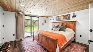 Ein Schlafzimmer mit einem Holzbett, einem großen Fenster und Blick ins Freie.