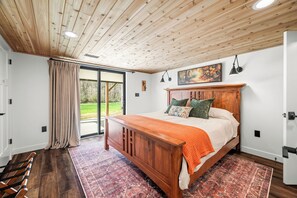 Ein Schlafzimmer mit einem Holzbett, einem großen Fenster und Blick ins Freie.