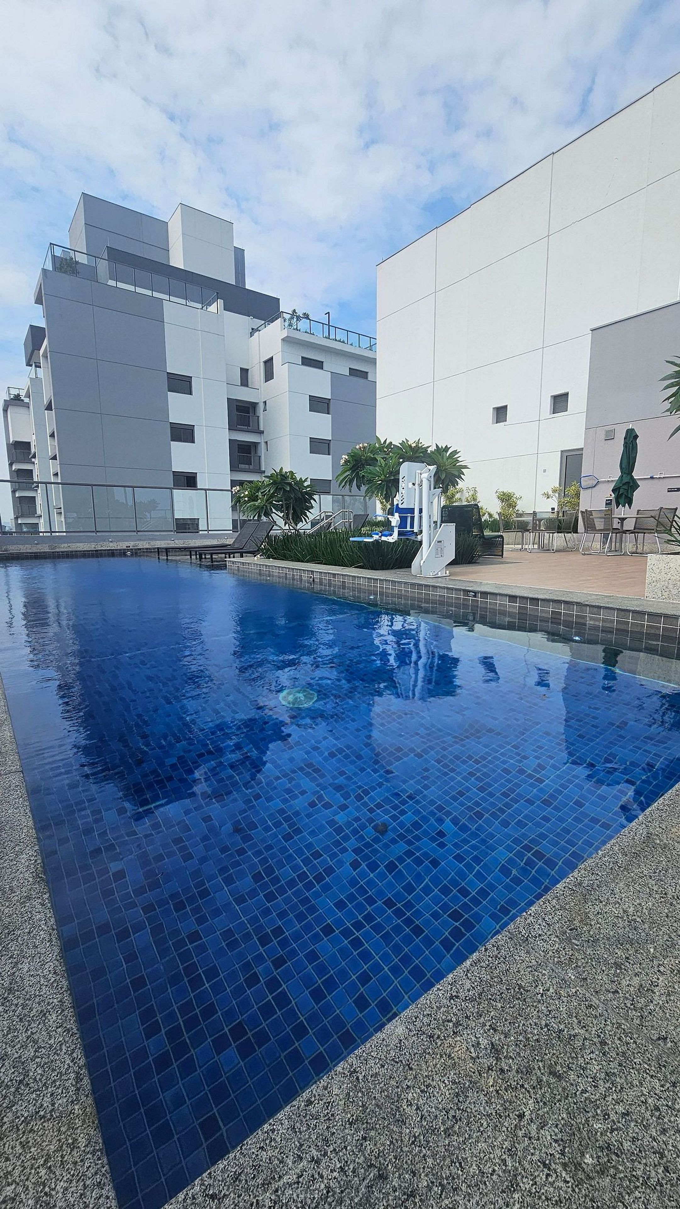 Une piscine dont les bords sont recouverts de carreaux, entourée d’un espace aménagé avec des plantes et du mobilier d’extérieur.