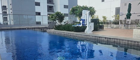 Une piscine dont les bords sont recouverts de carreaux, entourée d’un espace aménagé avec des plantes et du mobilier d’extérieur.