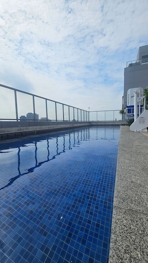 A swimming pool with a tiled edge, a metal railing, and a building in the background. - Condominio Hub Brooklin (São Paulo)