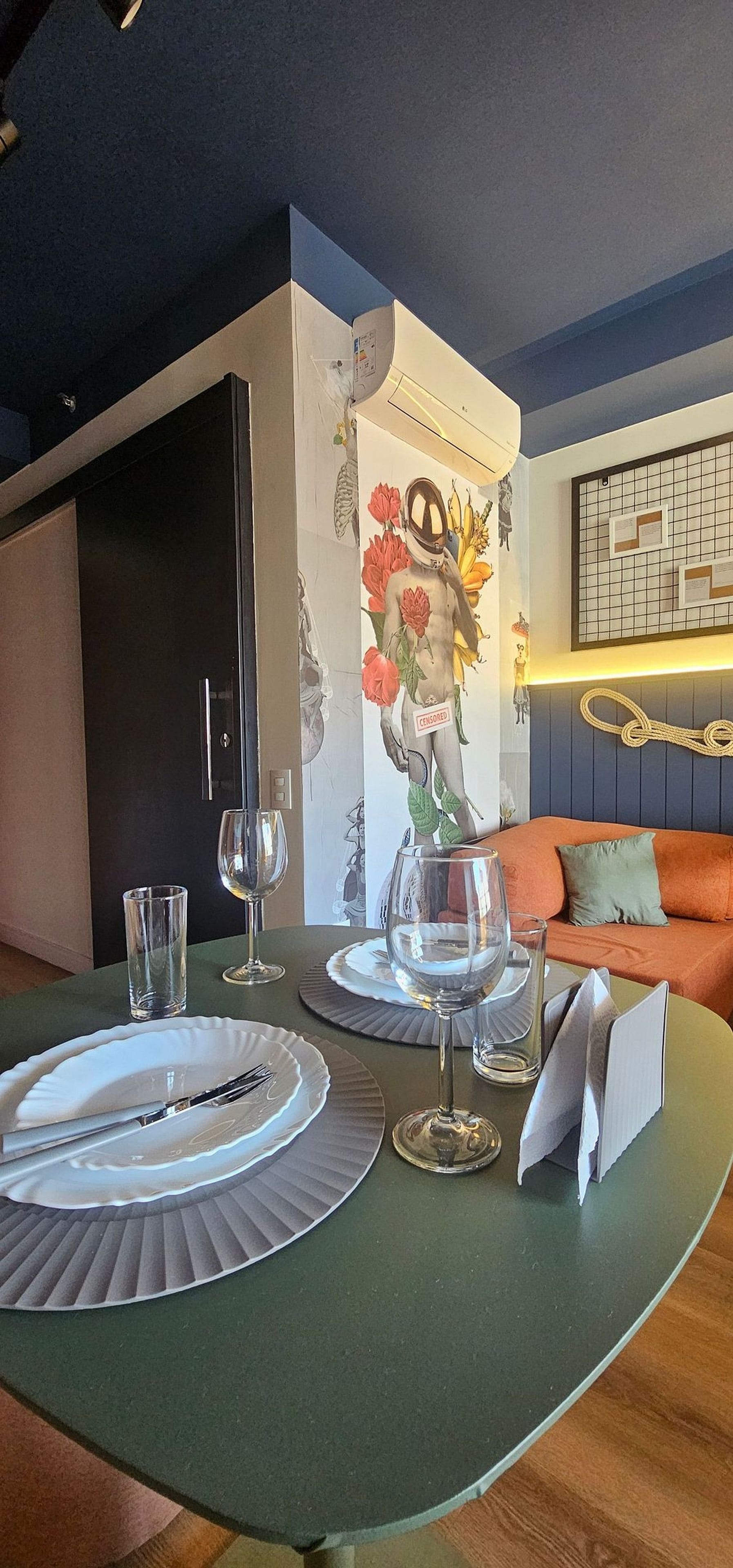 A dining area with a table set for two, a vase of flowers, and a wall with a grid pattern and a rope.