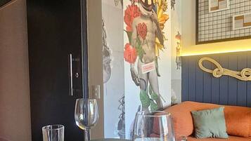 Uma área de refeições com uma mesa posta para dois, um vaso de flores e uma parede com padrão quadriculado e uma corda.